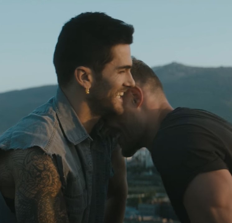 two men laugh and hug against a background of mountains and city