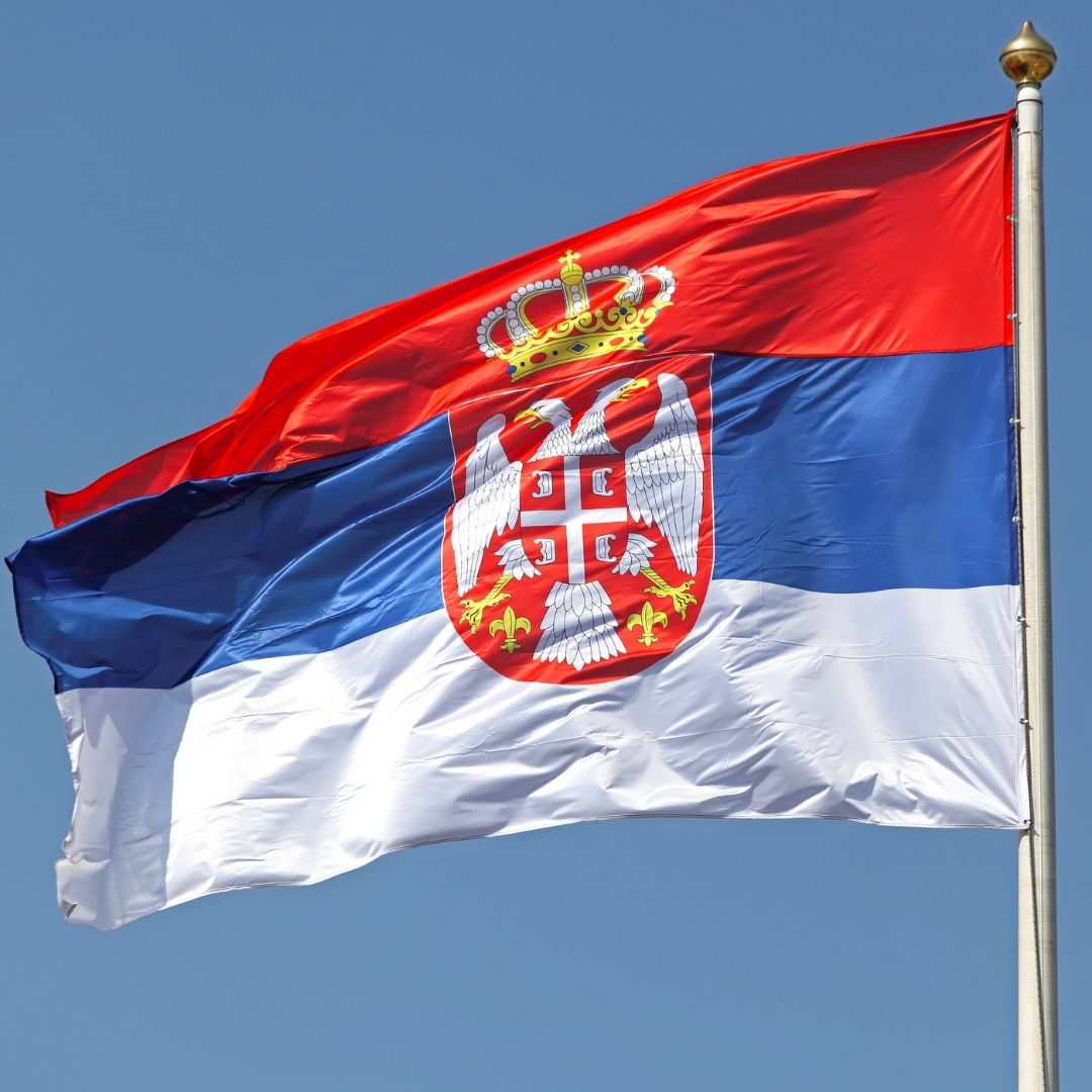 The flag of Serbia flies against a blue sky