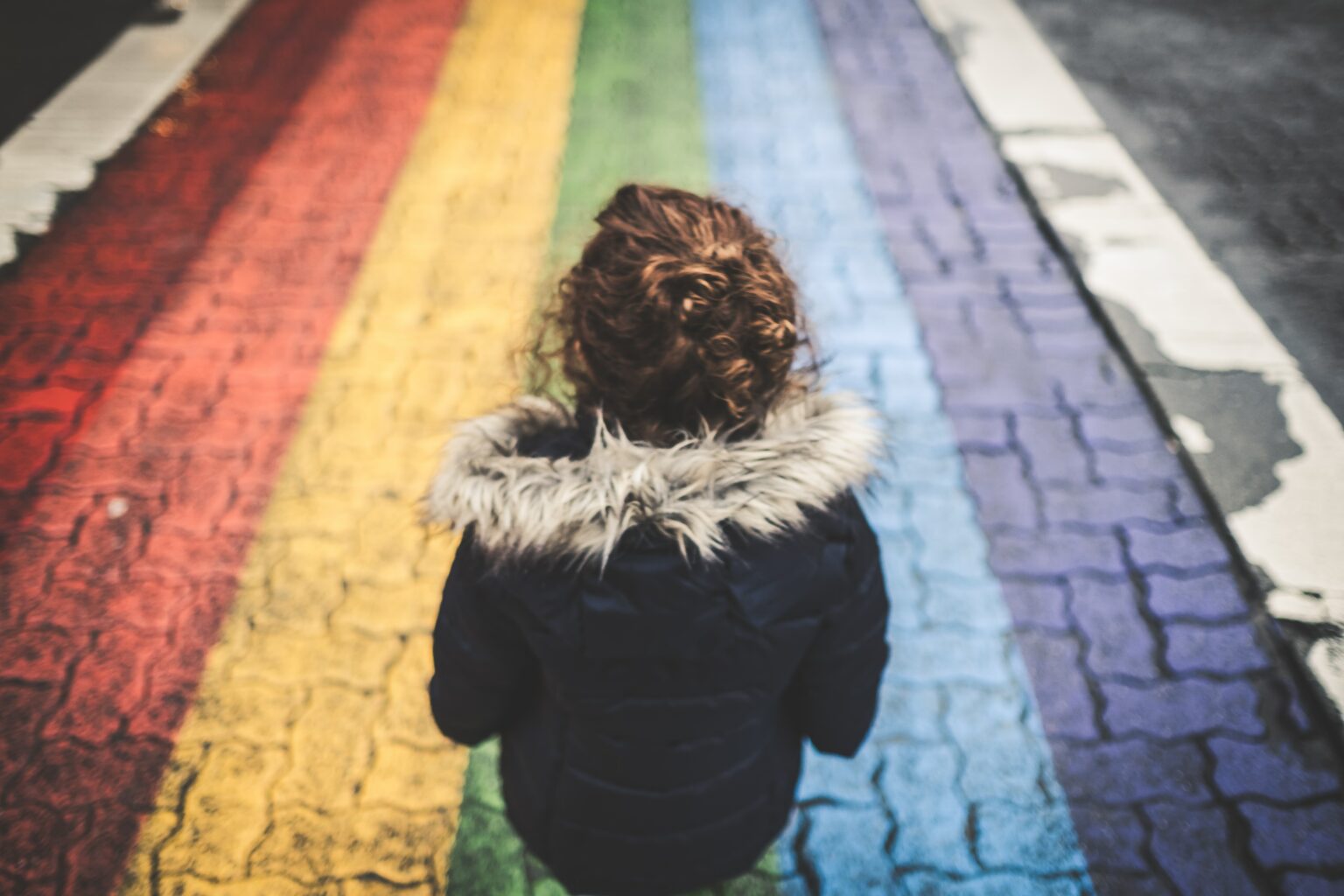 A child stands before a crossing in rainbow colors.
