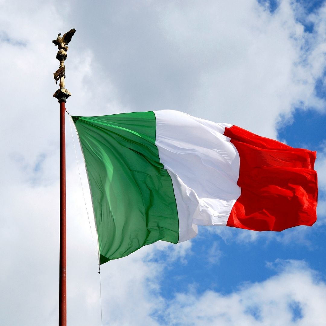 The Italian flag flies against a cloudy summer sky