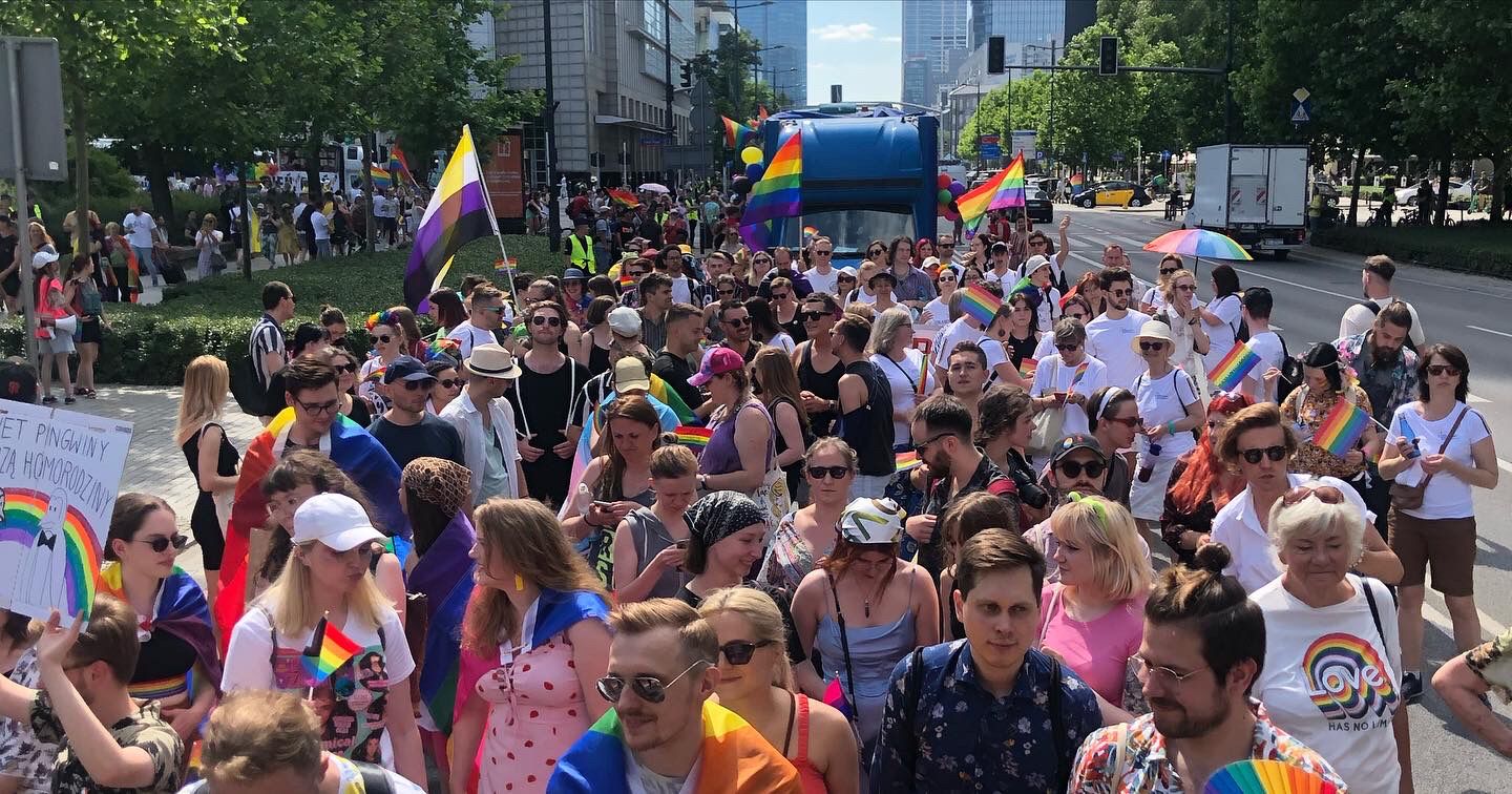 A large group of people marching together in Warsaw and waving rainbow flags