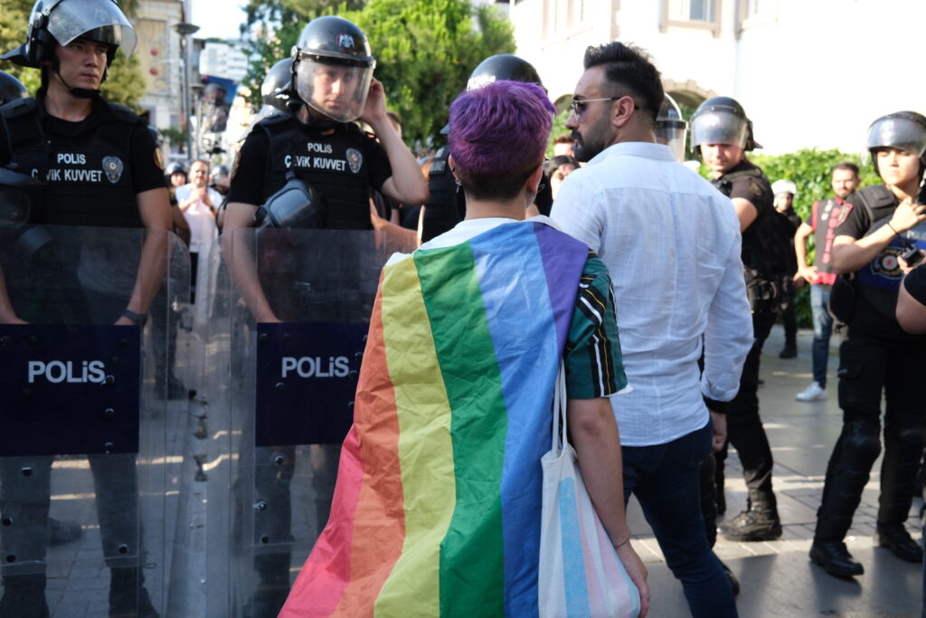 An activist covered in a rainbow flag marches towards a line of police officers