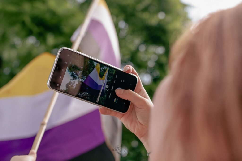 A non-binary flag and a person holding a smartphone. taking a picture of it.