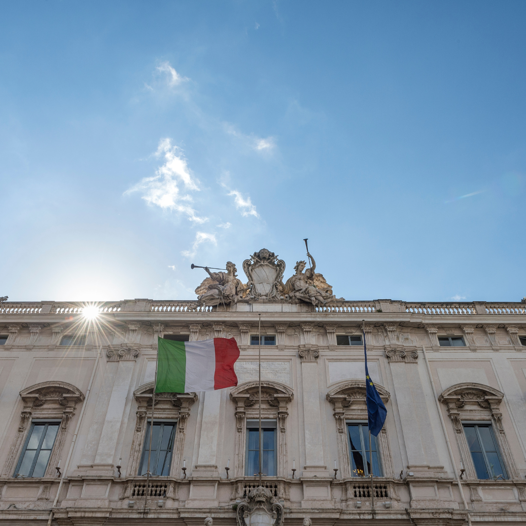 We see a blue sky above the Italian constitutional court building. An Italian flag flies in front